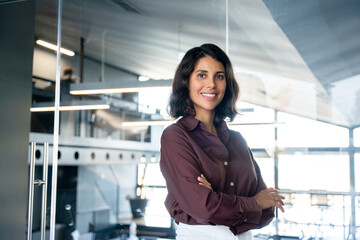 Portrait of beautiful successful hispanic young business woman with crossed arms smiling at camera....