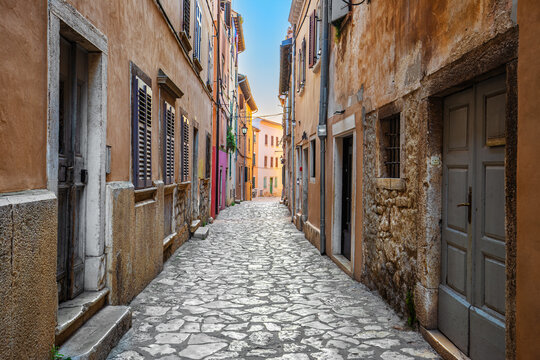 Fototapeta Rovinj, Croatia - Empty narrow street at the Old Town of Rovinj in a sunny summer morning with traditional cobblestones, colorful houses, windows and doors