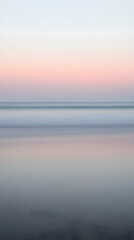 Obraz premium A long exposure shot of the ocean at sunset, creating a blurred effect with soft pink, white, and blue hues.