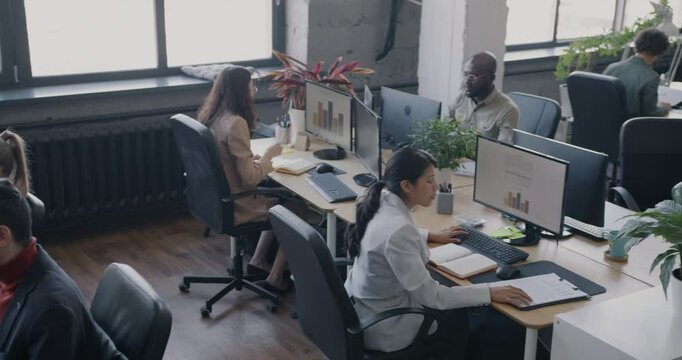 High angle view of busy coworking center with diverse group of people employees working at desks. Office workers and successful business concept.