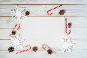 Christmas decorations and A4 sheet on a wooden background:  balls, branches, snowflakes and candy canes, top view, copyspace