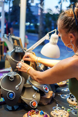 Mature Woman Organizing Display of Handmade Aluminum Wire Jewelry at Outdoor Market Stall
