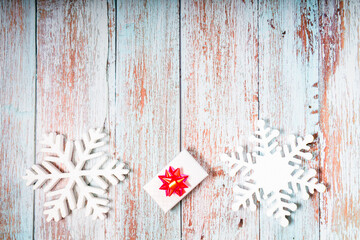 White decorative snowflakes and giftbox on white wooden background, copy space