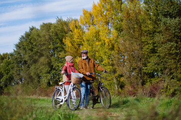 Elderly couple on a walk in the forest, pushing their bikes side by side. Seniors in love on stroll through autumn nature, enjoying a peaceful moment together.