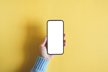Hand of woman showing smartphone with white blank screen mock-up on yellow empty background