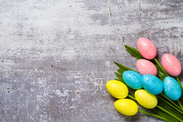 Easter background with copyspace. Colorful tulips and decorative eggs on concrete, top view
