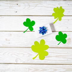 Green four leaf clovers and giftbox on white wooden background top view. Happy St. Patrick's Day...
