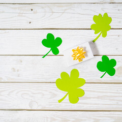 Green four leaf clovers and giftbox on white wooden background top view. Happy St. Patrick's Day...
