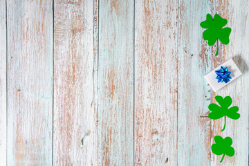 Green four leaf clovers and giftbox on white wooden background top view. Happy St. Patrick's Day greetings