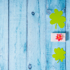 Green four leaf clovers and giftbox on white wooden background top view. Happy St. Patrick's Day...