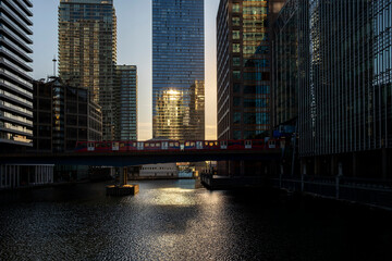 A cityscape view at sunset with golden reflections dancing on water bodies surrounded by towering skyscrapers, creating a tranquil yet vibrant urban environment in London UK