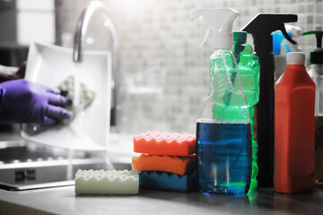 A white bottle with dishwashing gel on the background of a sink with dirty dishes and pouring water from a tap.