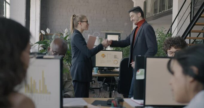 Young woman manager hiring new employee shaking hands showing workplace while colleagues clapping hands welcoming worker. Recruitment and career concept.