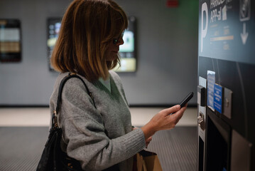 Close-up of a woman driver standing in front of a parking machine and paying with smartphone