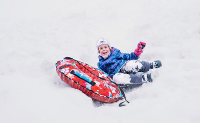Happy girl slid down a snow tube and funny fell from it. Winter fun, leisure. Hello winter