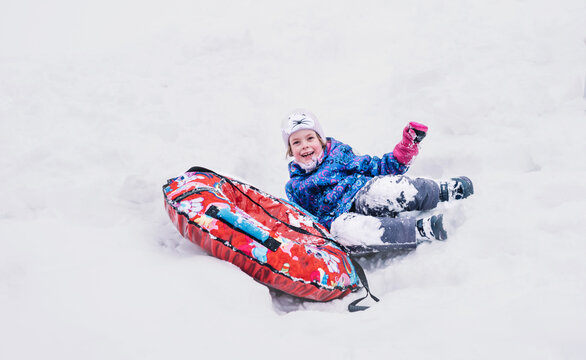Happy girl slid down a snow tube and funny fell from it. Winter fun, leisure. Hello winter
