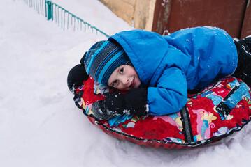 Portrait of a happy smiling boy on a snow tube in winter. Winter fun, leisure. Hello winter