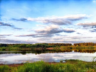 Serene landscape of a calm river reflecting clouds and greenery during sunset