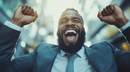 A businessman in a suit enthusiastically raises his hands in triumph, exuding joy and celebration amidst a blurred background, symbolizing achievement and success.