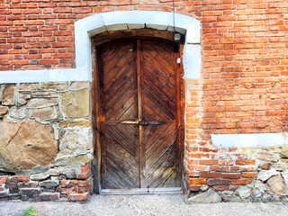Rustic wooden door embedded in a textured brick wall in an old building during daylight