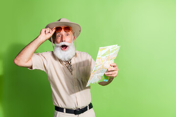 Photo of amazed old man touch sunglass hold map for traveling wear safari suit isolated green color background