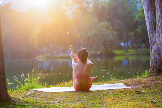 Young woman practicing yoga on soft green grass beside the lake. Young woman practicing yoga in nature. Healthy lifestyle. Concept of vitality, balance, mindfulness, Zen energy, calmness, relaxation, 