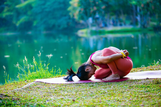 Young woman practicing yoga on soft green grass beside the lake. Young woman practicing yoga in nature. Healthy lifestyle. Concept of vitality, balance, mindfulness, Zen energy, calmness, relaxation, 