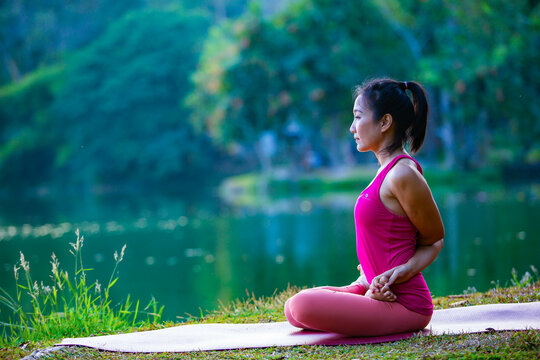 Young woman practicing yoga on soft green grass beside the lake. Young woman practicing yoga in nature. Healthy lifestyle. Concept of vitality, balance, mindfulness, Zen energy, calmness, relaxation, 