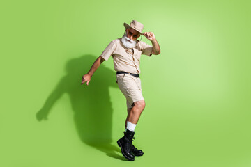 Elderly man in safari outfit poses against a vivid green backdrop, showcasing adventure and exploration lifestyle