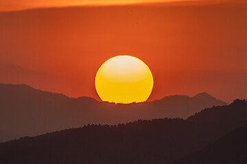 Fototapeta premium 夕焼けの中、山に沈む太陽