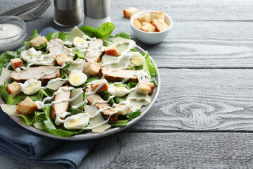 Delicious Caesar salad with chicken on grey wooden table, closeup. Space for text