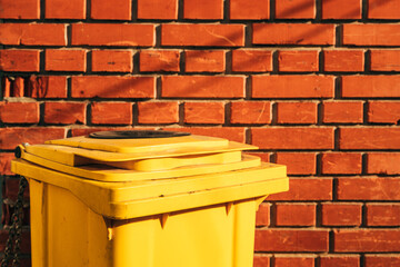 Yellow plastic trash bin against brick wall