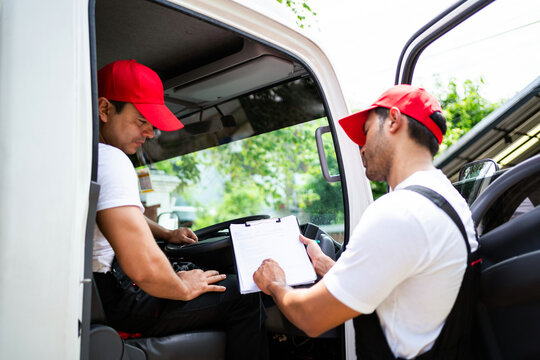 Happy professional truck driver with his assistant wearing a red cap smiling and talking about the parcel with checklists and location to deliver. A truck driver for home mover and delivery concept