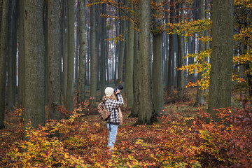 Woman with camera is photographing forest during autumn hiking. Outdoors adventure