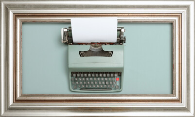 Top down view of old-fashioned pale cyan typewriter machine inside silver picture frame on pastel cyan surface with paper inside. © Sceliano