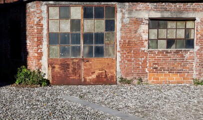 Exterior of long time abandoned workshop with brick wall,rusty door and weathered glasses....