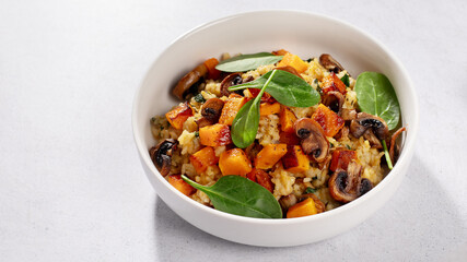 A vegan risotto with roasted pumpkin, mushrooms, and fresh spinach served in a white bowl on a light background