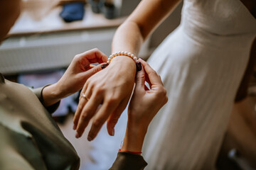 A close-up of a woman helping the bride put on a pearl bracelet, capturing a delicate moment of preparation and elegance before the wedding ceremony..