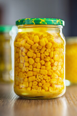 Canned sweet corn in jar on wooden table.