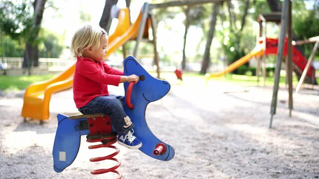 Little girl swings on a swing-spring at the playground holding the handles. High quality 4k footage