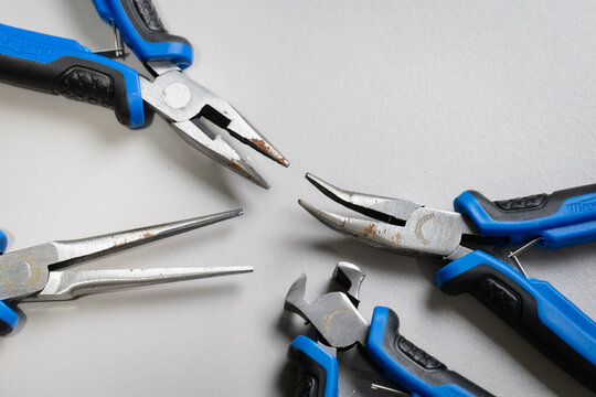 Different sets of pliers, needle nose, Nail puller, combination pliers, bent nose pilers with blue and black handle with some metal showing rust