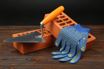 Red bricks, putty knife and rubber gloves on wooden table. Building material
