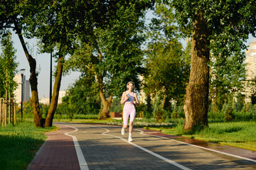 A joyful young woman jogs along a winding path in a lush green park.