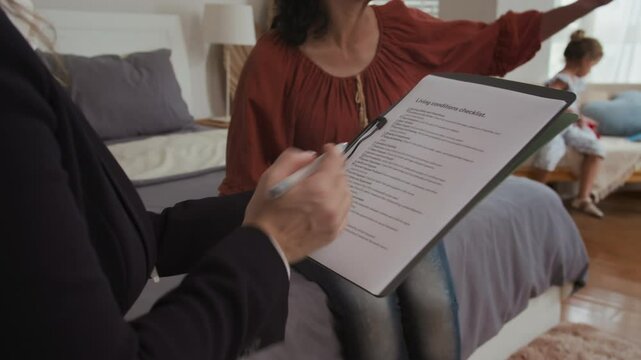Cropped shot of unrecognizable social worker filling form while listening to mother talking about living conditions with daughter at home