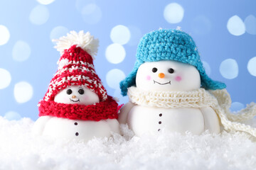Cute decorative snowman on artificial snow against light blue background with blurred lights, closeup