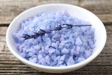 Natural sea salt in bowl and lavender on wooden table, closeup