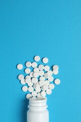 Various medicines and health pills poured from a medical white bottle, healthcare and medical top view on a colorful blue background.
