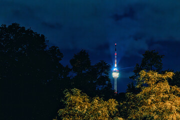 Hell erleuchteter Stuttgarter Fernsehturm bei Nacht scheint zwischen Bäume hindurch © tom-pic-art