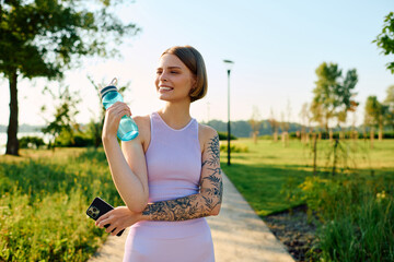 A joyful young woman relaxes in a sunny park, sipping water.