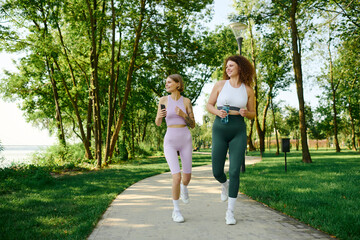 Fototapeta premium Two women enjoy jogging side by side in a vibrant green park.